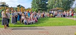 Attēlā redzami bērni ar skolotājām, stāv pasākumā.