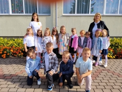 Attēlā redzami bērni ar skolotājām, skatoties uz kameru.