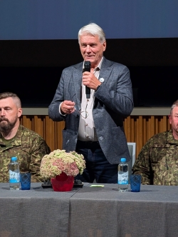 Attēlā redzams vīrietis, kurš runā mikrofonā.