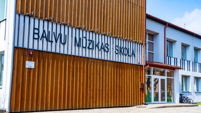 Attēlā redzama Balvu Mūzikas skolas fasāde. Gaiša ēka ar koka elementiem un skolas uzrakstu.