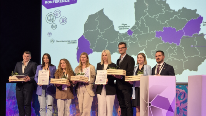 Projekta "Digitālā darba ar jaunatni sistēmas attīstība pašvaldībās" noslēguma konferences dalībnieki uz skatuves ar apbalvojumiem un diplomiem rokās. Fonā ekrāns ar Latvijas karti un uzrakstu "SADARBĪBAS MEISTARI".