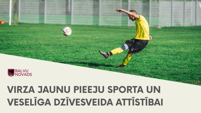 Futbolists dzeltenā t-kreklā un melnās šortos spēles gaitā sper pa futbola bumbu uz zaļa zālāja laukuma. Fonā redzams nožogojums un vārti.