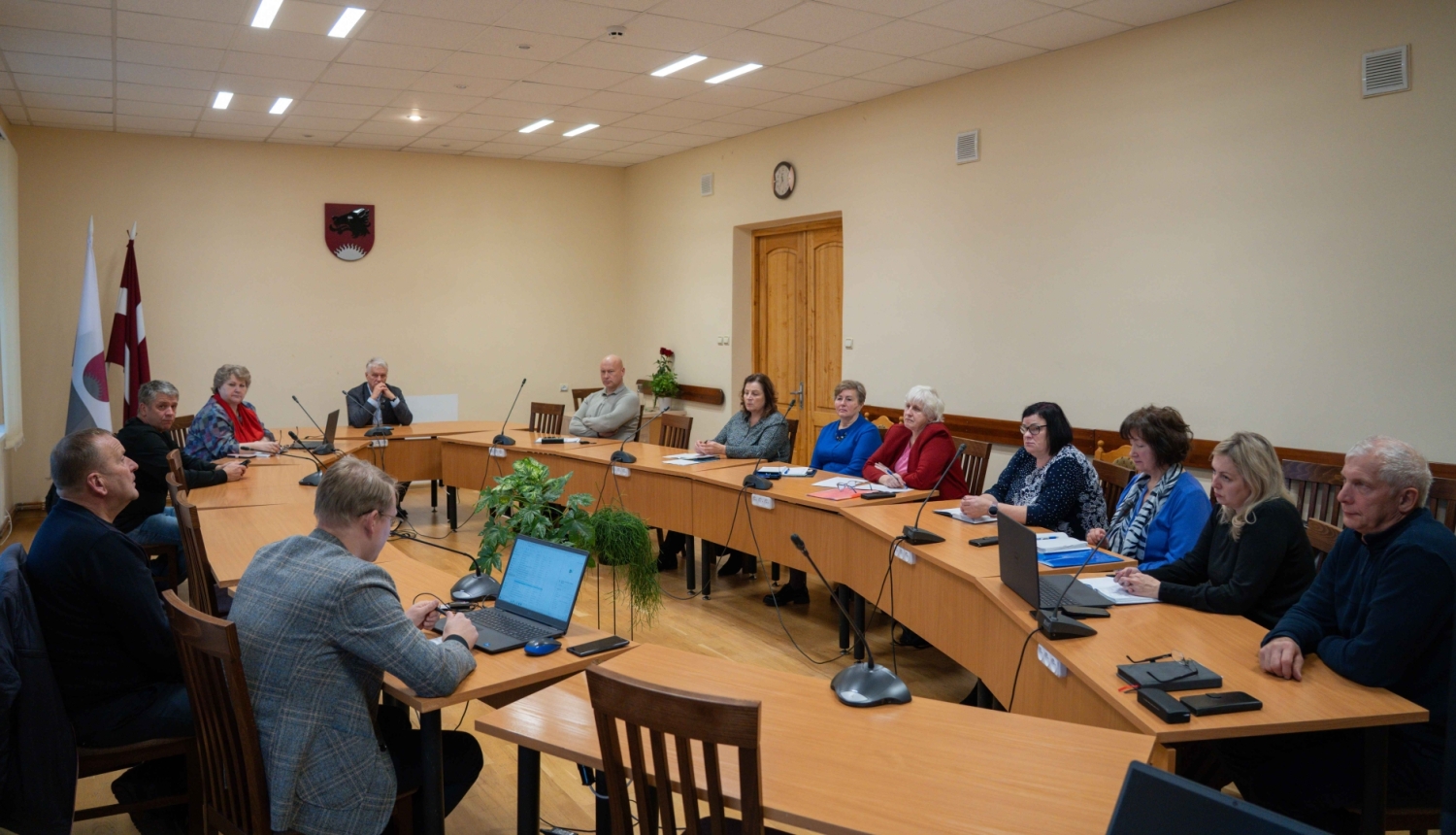 Attēlā redzami cilvēki, kas sēž pie galda un runā