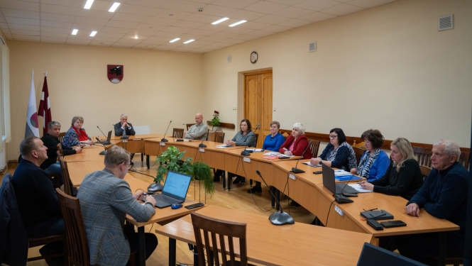 Attēlā redzami cilvēki, kas sēž pie galda un runā