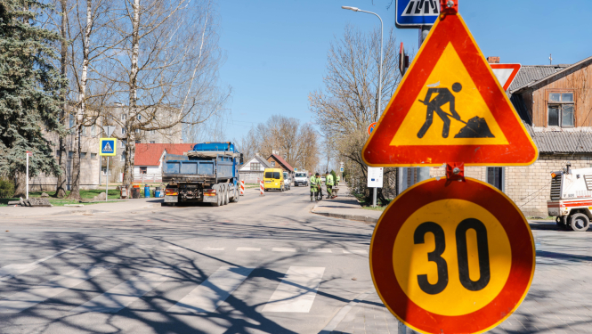 Ceļa remontdarbi Baznīcas ielā – redzamas brīdinājuma zīmes par ceļa darbiem un ātruma ierobežojumu 30 km/h, fonā strādā tehnika un darbinieki.