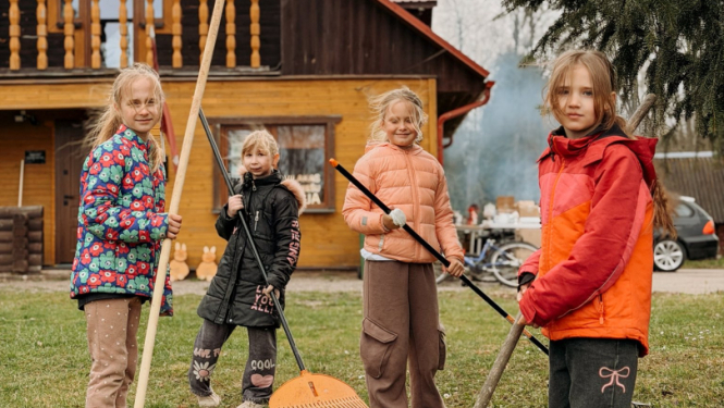 Meitenes ar grābekļiem rokās grāpj lapas pie Viļakas jauniešu mājas
