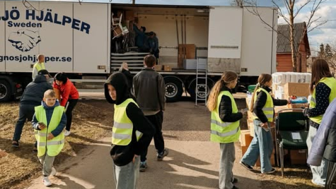 Jaunieši drošības vestēs palīdz izkraut no furgona atvestās labdarības pakas