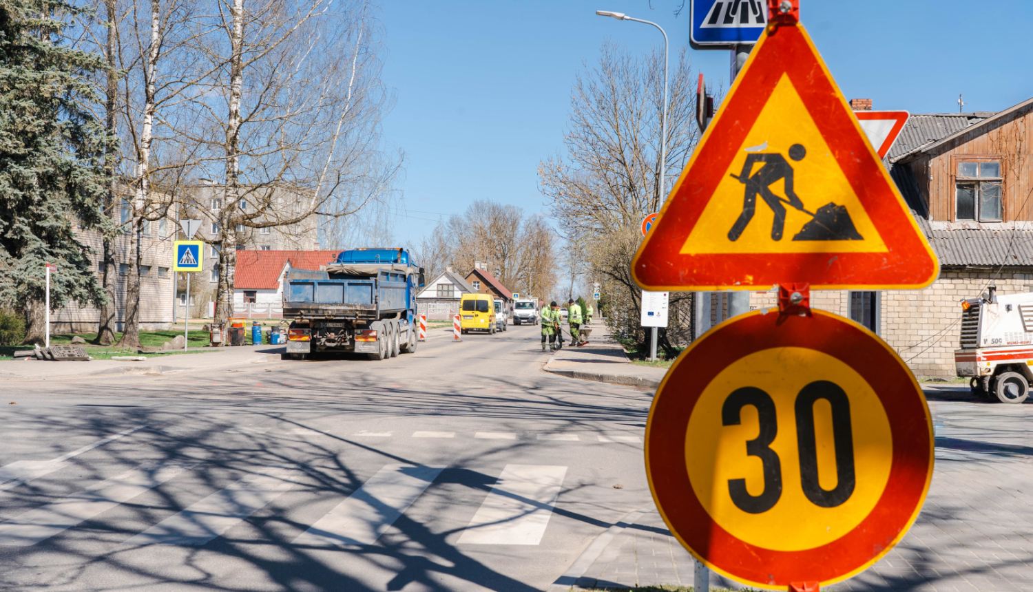 Ceļa remontdarbi Baznīcas ielā – redzamas brīdinājuma zīmes par ceļa darbiem un ātruma ierobežojumu 30 km/h, fonā strādā tehnika un darbinieki.