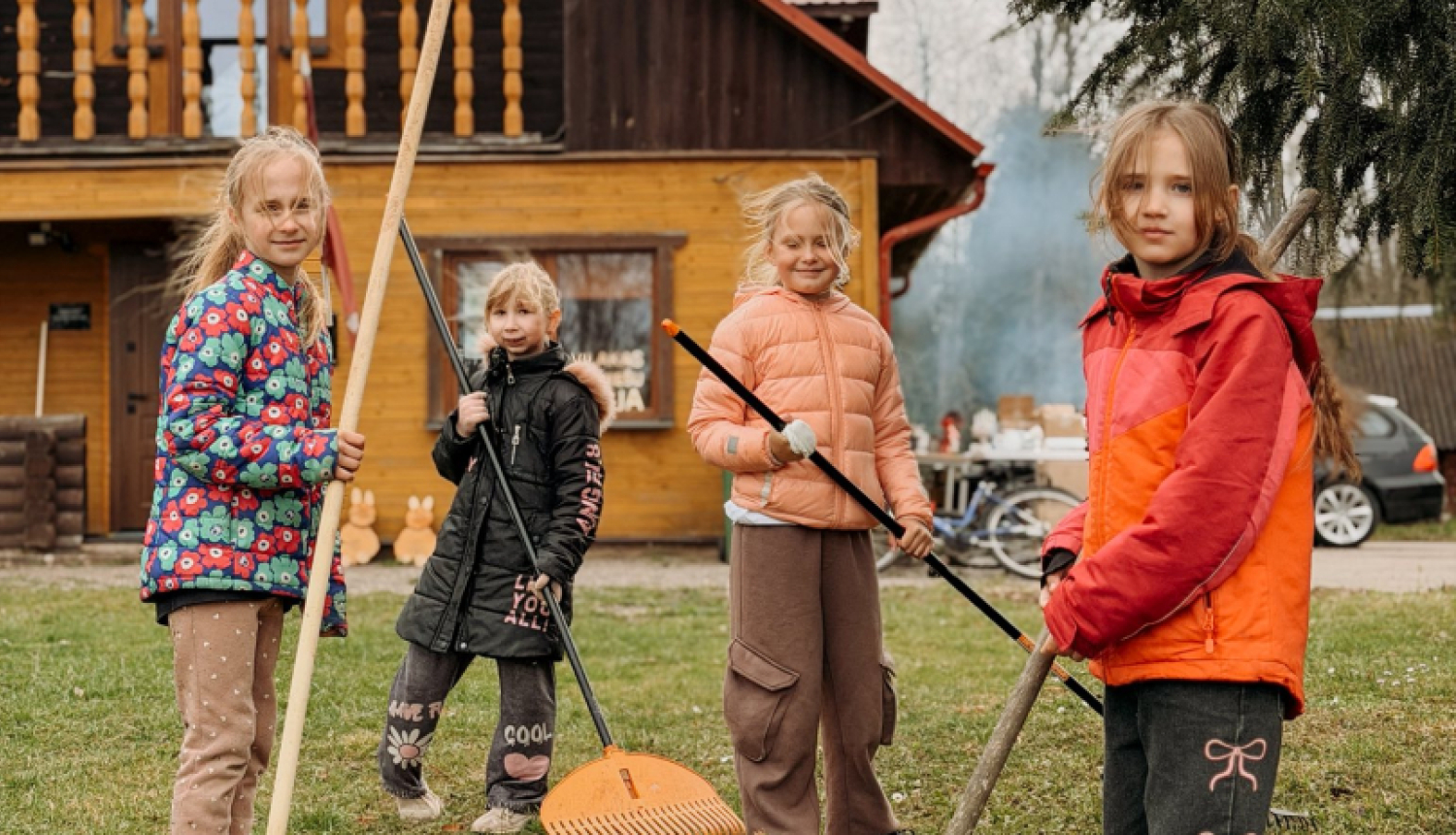 Meitenes ar grābekļiem rokās grāpj lapas pie Viļakas jauniešu mājas